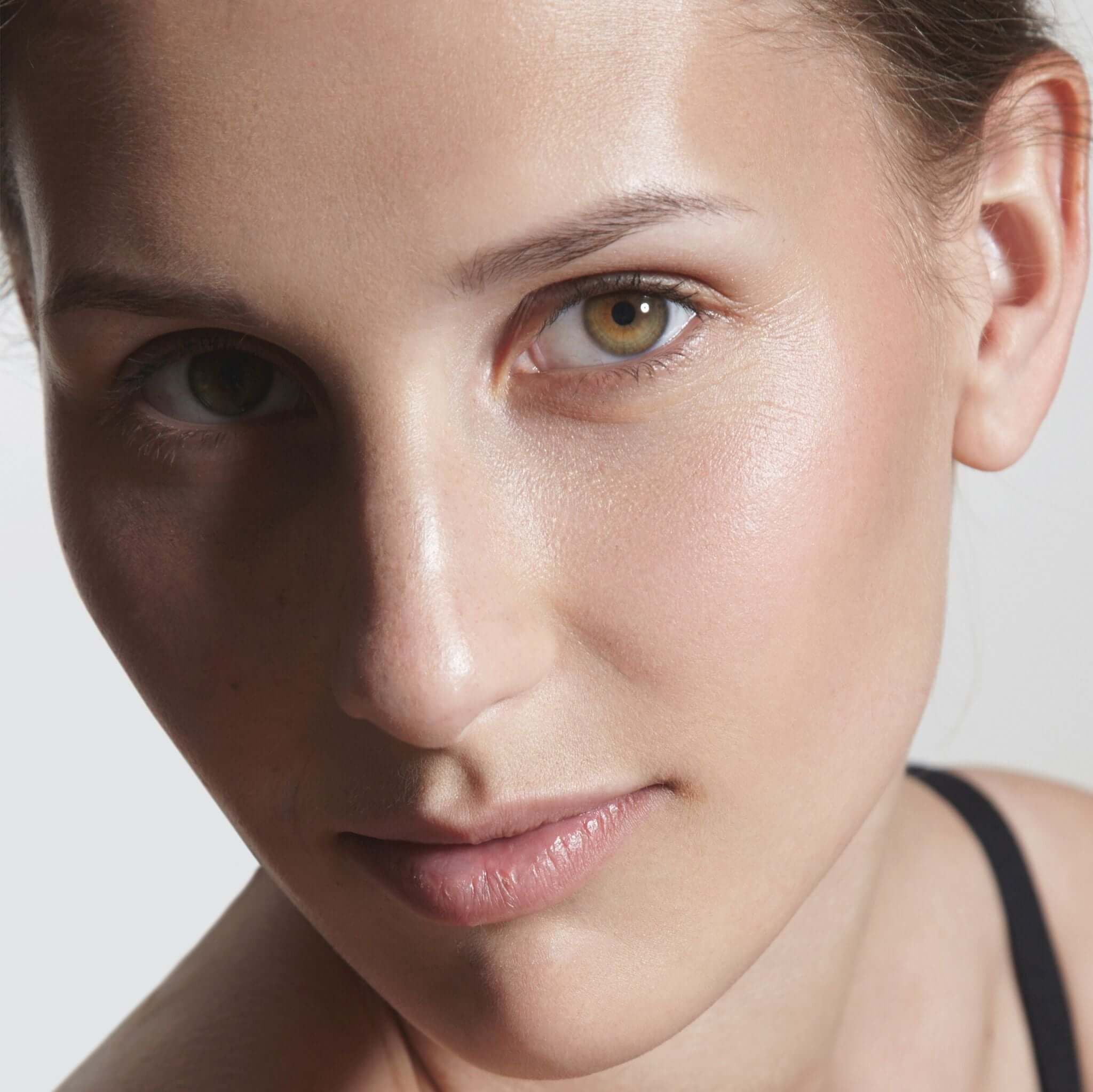 Close-up of a woman showcasing natural skin, highlighting her glowing complexion and expressive eyes.