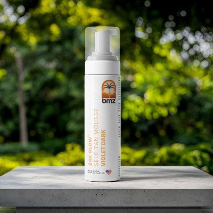 24K Glow self-tan mousse bottle on a concrete surface surrounded by lush greenery, ideal for a radiant bronze look.